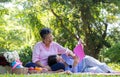 Asian daughter Sleeping on mother lap and reading book on picnic mat in the park. A happy senior woman talks with her daughter.