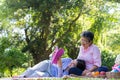 Asian daughter Sleeping on mother lap and reading book on picnic mat in the park. A happy senior woman talks with her daughter. Royalty Free Stock Photo