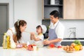 Asian daughters feeding salad to her mother and her father stand by when a family cooking in the kitchen at home. Family life love