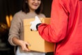 An Asian deliver man in red uniform handing parcel to a female costumer in front of the house. A postman and express delivery