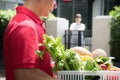 Asian delivery man in red uniform delivering  groceries box of food, fruit, vegetable and drink to woman recipient at home Royalty Free Stock Photo