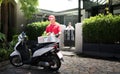 Asian delivery man in red uniform delivering  groceries box of food, fruit, vegetable and drink to woman recipient at home Royalty Free Stock Photo