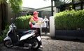 Asian delivery man in red uniform delivering  groceries box of food, fruit, vegetable and drink to woman recipient at home Royalty Free Stock Photo