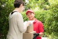 Asian delivery man in red uniform delivering parcel box to woman recipient at home Royalty Free Stock Photo