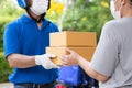 Asian delivery man wearing face mask and blue uniform with motorcycle delivering parcel box express service to woman customer Royalty Free Stock Photo