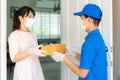 Asian delivery man wearing face mask and glove in blue uniform holding a cardboard boxes in front house and woman accepting a Royalty Free Stock Photo