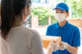 Asian delivery man wearing face mask and glove in blue uniform holding a cardboard boxes in front house and woman accepting a Royalty Free Stock Photo