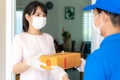 Asian delivery man wearing face mask and glove in blue uniform holding a cardboard boxes in front house and woman accepting a Royalty Free Stock Photo