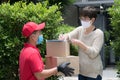 Asian delivery man wearing face mask and gloves in red uniform delivering parcel box to recipient during COVID-19 outbreak