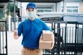 Asian Delivery man wearing mask send a package carton thumb up on front receiver shipping deliver Royalty Free Stock Photo