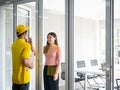 Asian delivery man who wear yellow uniform with cap hold confidential document in craft paper and knock the window for send