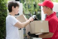 Asian delivery man in red uniform delivering parcel box to woman recipient at home with recipient sign to receive the package on s Royalty Free Stock Photo