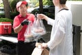 Asian delivery man in red uniform delivering shopping bags of food and drink to woman recipient at home Royalty Free Stock Photo