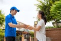 Asian delivery young man in blue uniform smile and holding a cardboard boxes in front house and Asian woman accepting a delivery