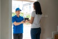 Asian delivery young man in blue uniform smile and holding food boxes in front house and Asian woman accepting a delivery of food Royalty Free Stock Photo