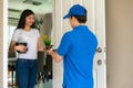 Asian delivery young man in blue uniform smile and holding food boxes in front house and Asian woman accepting a delivery of food Royalty Free Stock Photo