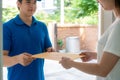 Asian delivery young man in blue uniform smile and holding letter or document envelope in front house and Asian woman accepting a