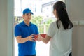 Asian delivery young man in blue uniform smile and holding pizza boxes in front house and Asian woman accepting a delivery of Royalty Free Stock Photo