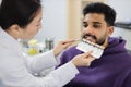 Asian dentist checking and selecting color of young bearded man teeth. Royalty Free Stock Photo