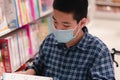 Disabled child on wheelchair wearing a mask reading a book from shelves in books store or school library