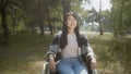 An asian disabled female with long hair is posing, sitting in a wheelchair in a public park, smiling and touching hair