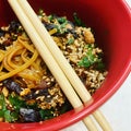 Asian dish in a red bowl, wooden sticks, sesame and small pieces of algae, long noodles and peanuts, Korean food, Asian dish