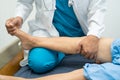 Asian doctor physiotherapist examining, massaging and treatment knee and leg of senior patient in orthopedist medical clinic nurse