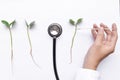 Asian doctor`s hand, stethoscope, glass thermometer and three sprouts.