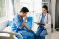 Asian doctor in white suit take notes while discussing and Asian elderly, man patient who lying on bed with receiving saline Royalty Free Stock Photo