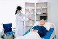 Asian doctor in white suit take notes while discussing and Asian elderly, man patient who lying on bed with receiving saline Royalty Free Stock Photo