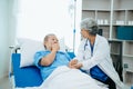 Asian doctor in white suit take notes while discussing and Asian elderly, man patient who lying on bed with receiving saline Royalty Free Stock Photo