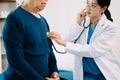 Asian doctor in white suit take notes while discussing and Asian elderly, man patient who lying on bed with receiving saline Royalty Free Stock Photo