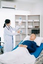 Asian doctor in white suit take notes while discussing and Asian elderly, man patient who lying on bed with receiving saline Royalty Free Stock Photo