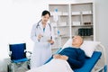 Asian doctor in white suit take notes while discussing and Asian elderly, man patient who lying on bed with receiving saline Royalty Free Stock Photo