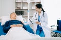 Asian doctor in white suit take notes while discussing and Asian elderly, man patient who lying on bed with receiving saline Royalty Free Stock Photo