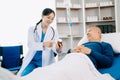 Asian doctor in white suit take notes while discussing and Asian elderly, man patient who lying on bed with receiving saline Royalty Free Stock Photo