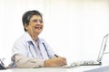 Asian doctor woman using a laptop computer and writing something on clipboard at hospital desk office. Royalty Free Stock Photo