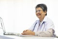 Asian doctor woman using a laptop computer and writing something on clipboard at hospital desk office. Royalty Free Stock Photo