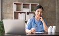 Asian doctor young beautiful woman smiling using working with a laptop computer and her writing something on paperwork Royalty Free Stock Photo