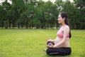 Asian Eastern Chinese happy beautiful pregnant woman do yoga sit in meditation in nature outdoor sit on green grass meadow park Royalty Free Stock Photo