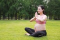 Asian Eastern Chinese pregnant woman do yoga sit in meditation in nature outdoor on grass meadow put her palms together devoutly Royalty Free Stock Photo