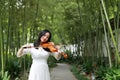 Asian Eastern Chinese young artist player woman play violin perform music closed eyes garden nature outdoor bamboo path