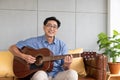 Asian elder man playing guitar at the sofa inside of the house. Active senior lifestyle after retirement with happiness Royalty Free Stock Photo