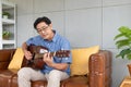 Asian elder man playing guitar at the sofa inside of the house. Active senior lifestyle after retirement with happiness Royalty Free Stock Photo