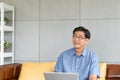 Asian elder senior man using computer laptop while sitting on sofa inside of the house for search and thinking about idea or Royalty Free Stock Photo