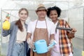 Asian elderly farmer hold watering can with two multiethnic teenager friend girls hold garden tools, standing at front of Royalty Free Stock Photo
