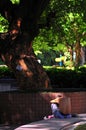 An Asian elderly sits on a bench crunch himself in a park in Hong Kong with dramatic light spot