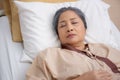 Asian elderly woman asleep on bed with surveillance in hospital ward, patient senior unconscious lying on bed.