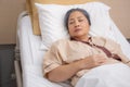 Asian elderly woman asleep on bed with surveillance in hospital ward, patient senior unconscious lying on bed.