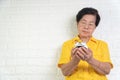 Asian elderly woman holding a white alarm clock, here face shows anxiety. The concept aging society That needs time and grandchild